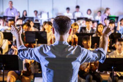 Male school conductor conductiong his student band to perform mu