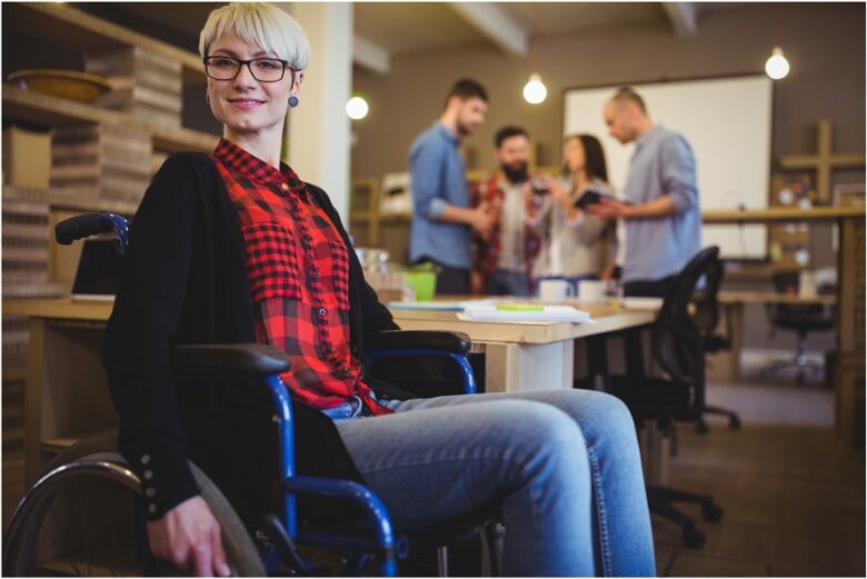 Portrait of confident woman on wheelchair while colleagues in background at creative office